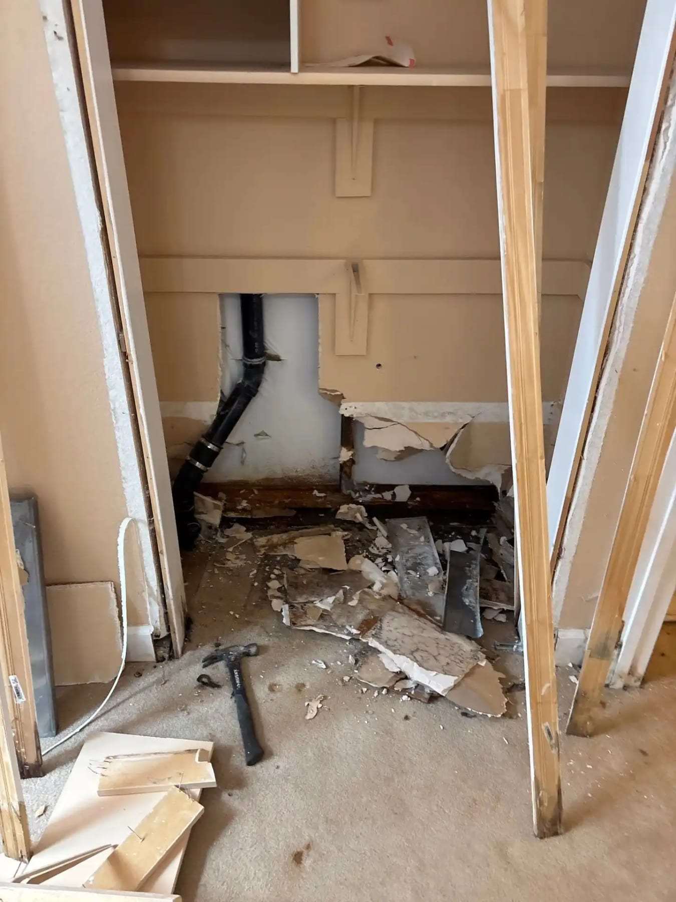 Kitchen cabinet base removed to expose the plumbing and a damaged wall