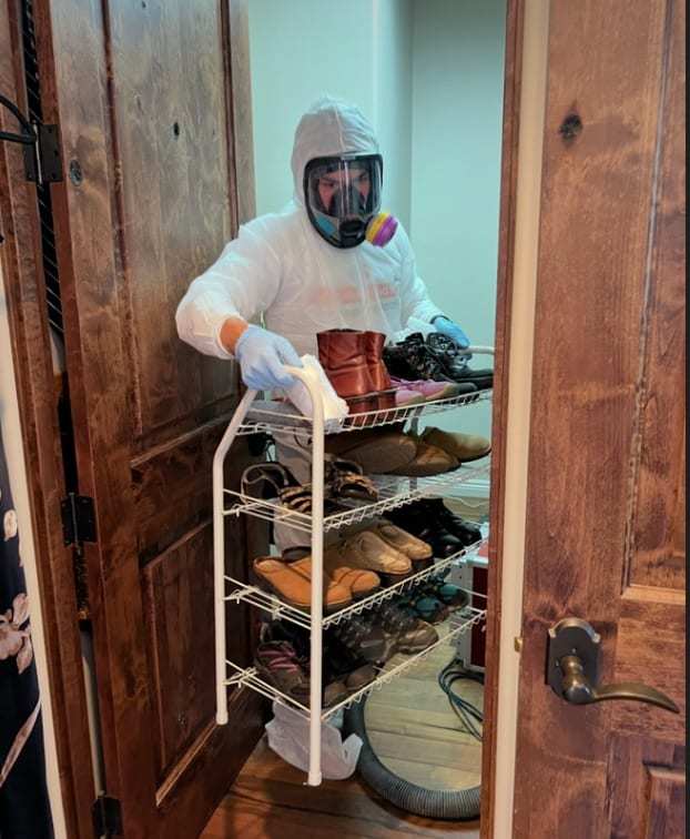 Technician in a protective suit and respirator cleaning shoes on a rack
